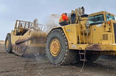 Motor scraper being pressure washed by two workers