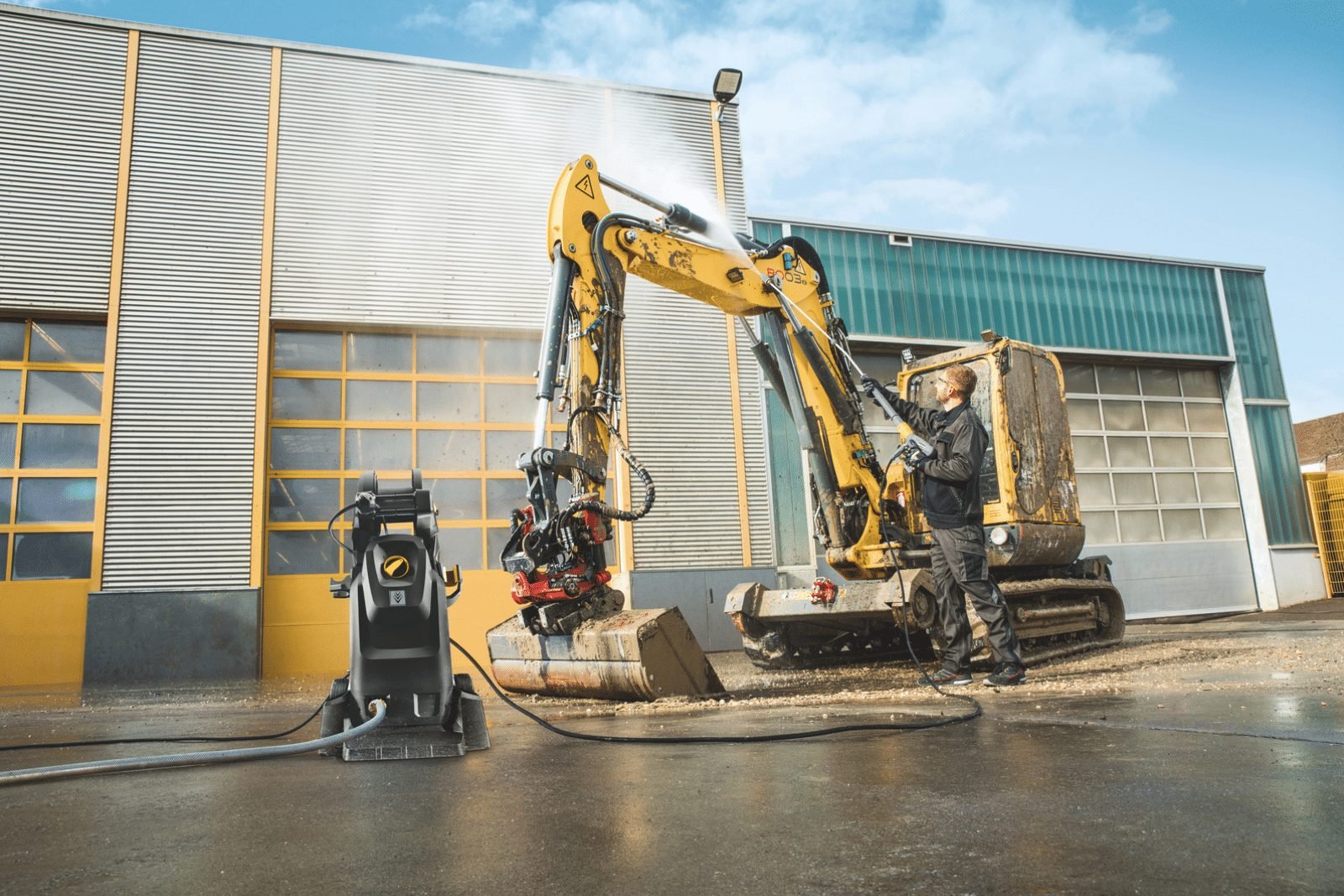 Excavator being pressure washed outside an industrial shop